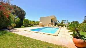 Una casa moderna con piscina, immersa in prati curati e piante in vaso.