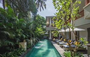 A pool with lounge chairs and umbrellas, surrounded by lush greenery. - Baale Resort Goa (Arpora)