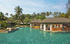 A clear pool with lounge chairs and umbrellas, surrounded by lush greenery and palm trees. - Baale Resort Goa (Arpora)