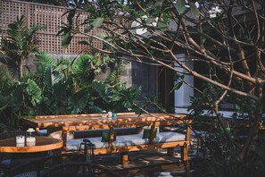 An outdoor seating area with wooden tables and chairs, surrounded by lush tropical plants and a wooden fence. - Baale Resort Goa (Arpora)