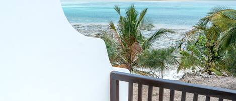 A balcony with a view of the beach, wooden furniture, and a wicker chair.