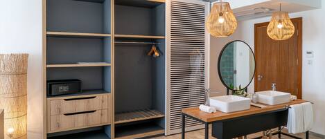 A modern bathroom with a wooden vanity, two sinks, a large mirror, and a walk-in closet with shelves and hanging space.