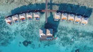 Vista aérea de bungalows sobre el agua con un edificio central, unidos por un puente.