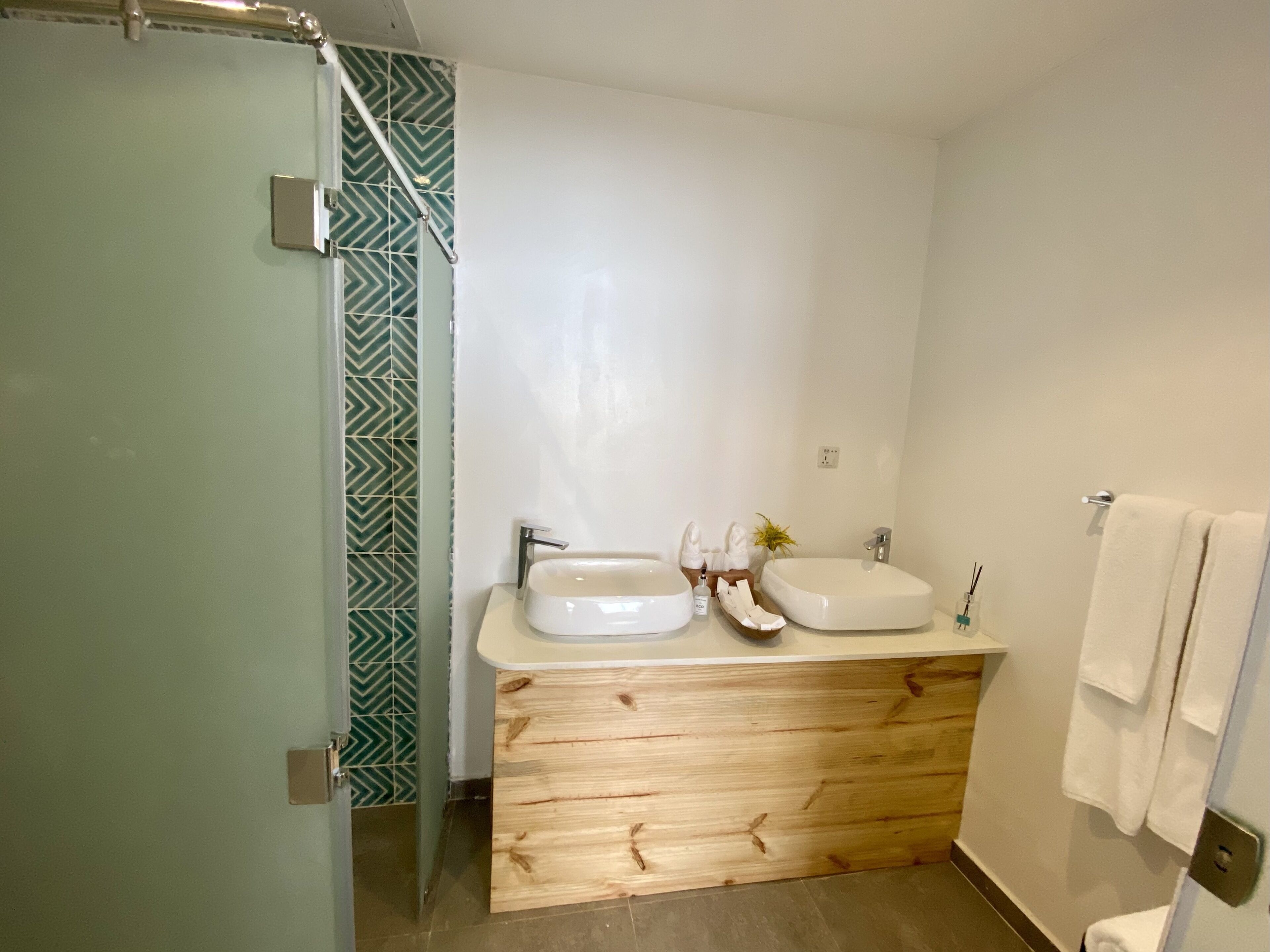 A modern bathroom with a glass shower enclosure, a wooden vanity with two sinks, and a towel rack.