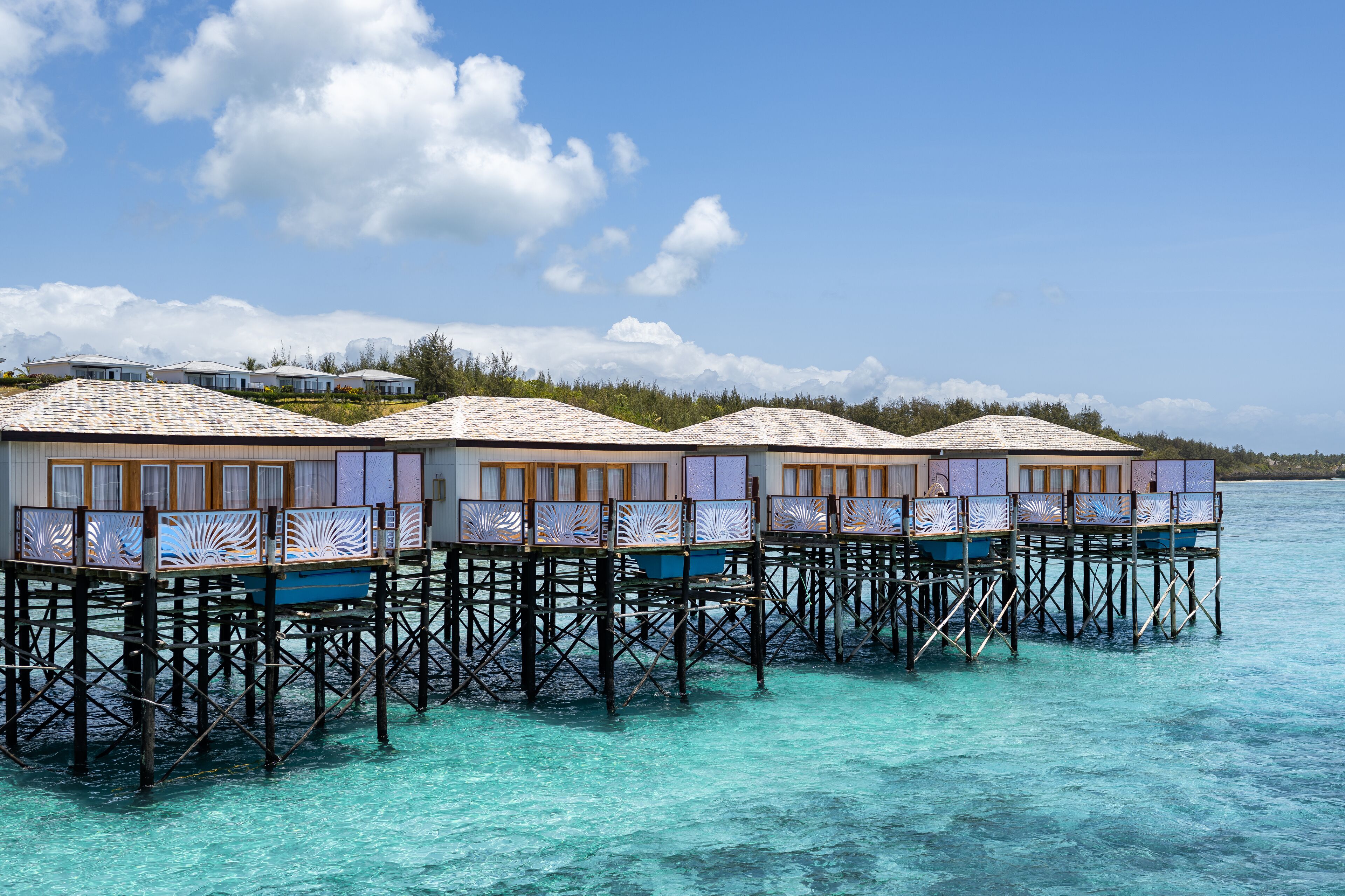Des bungalows sur pilotis dotés de balustrades en bois et offrant une vue dégagée sur la mer turquoise.
