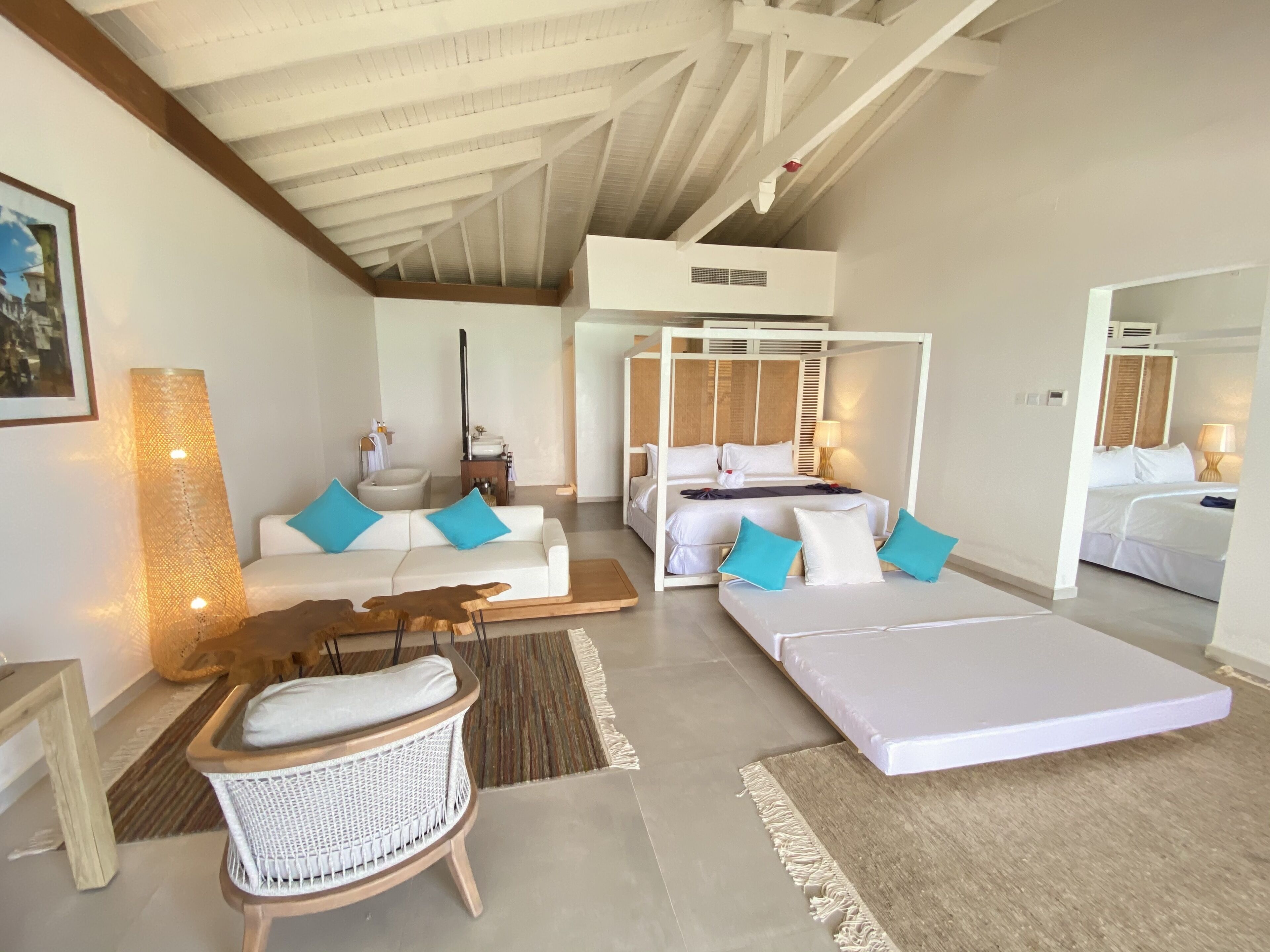 A spacious room with a large bed, a sofa, a wicker chair, and a small table.