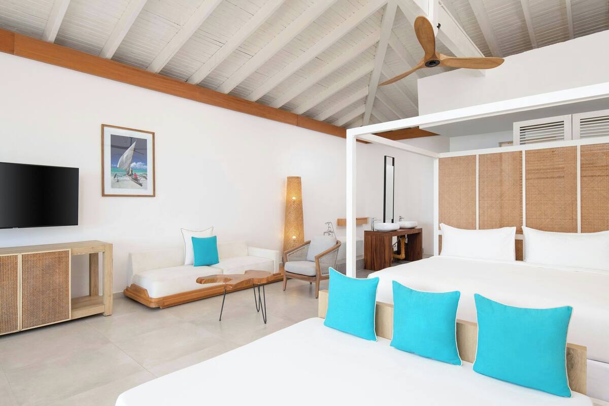 A modern hotel room with a large bed, a TV, a desk, and a window with a view of the sea.