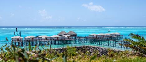 Bungalows sobre el agua con techos de paja, conectados por una pasarela de madera, con vistas a aguas turquesas.