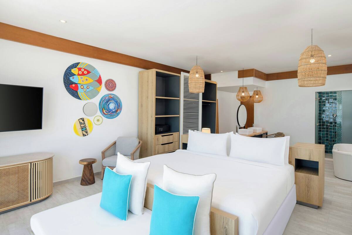 A modern hotel room with a large bed, a flat-screen TV, a wooden wardrobe, and a bathroom with a glass shower.