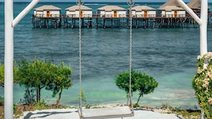 Una hamaca en la playa con vista al mar y cabañas sobre el agua.