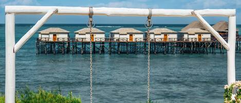 A beach swing overlooking a sea with overwater bungalows.