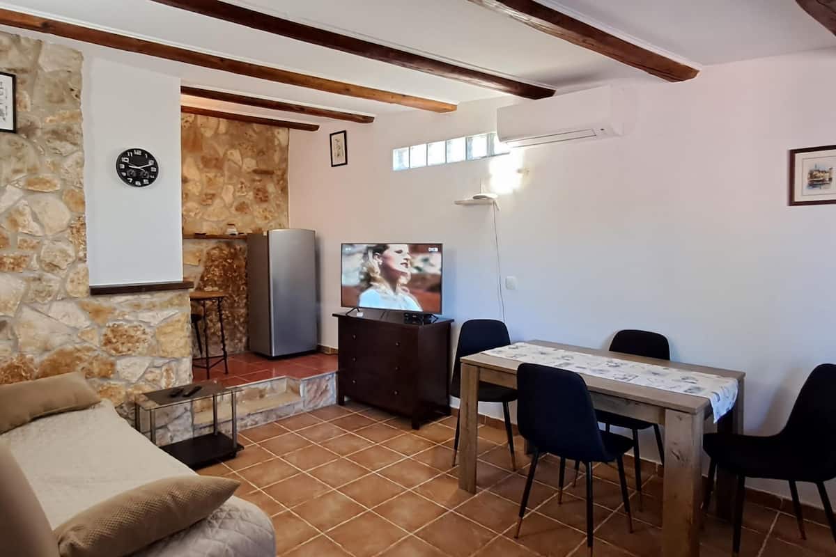 A living room with a stone wall, a sofa, a TV, and a dining table with chairs.