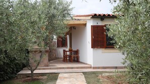 A patio area with a stone pathway leading to a wooden table and chairs, surrounded by olive trees and a white building with brown shutters. - Holiday Homes Marta (Rovinj)