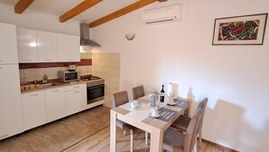 A compact kitchen with white cabinets, a microwave, stove, and a dining table with chairs. - Holiday Homes Marta (Rovinj)
