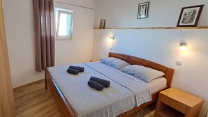 A neatly made bed with a striped bedspread and pillows, a wooden nightstand with a drawer, and a window with curtains. - Holiday Homes Marta (Rovinj)