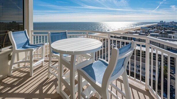 A balcony with a round table and white chairs, overlooking a beach and cityscape. - Four Bedroom Luxury Condo with Spectacular Ocean & Bay Views (Ocean City)