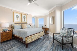 A bedroom with a bed, a chair, a desk, and a view of the ocean.
