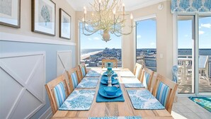 A dining room with a view of the city, a chandelier, and framed artwork on the wall. - Four Bedroom Luxury Condo with Spectacular Ocean & Bay Views (Ocean City)