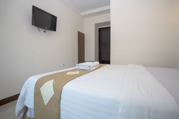 Habitación de hotel con una cama, un televisor montado en la pared y una puerta que da a otra habitación.