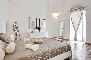 A bedroom with a bed, a bedside table, a mirror, a window with curtains, and a wall-mounted air conditioner.