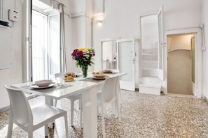 Uma sala de jantar com uma mesa branca, cadeiras e um vaso de flores.