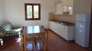 Cocina compacta con mesa y sillas, refrigerador y ventana con vista a follaje.