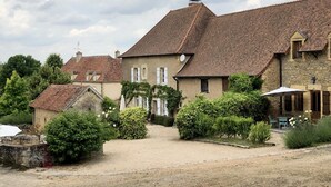 Ein großes Steinhaus mit Ziegeldach, umgeben von üppiger Vegetation und einer Schotterauffahrt.