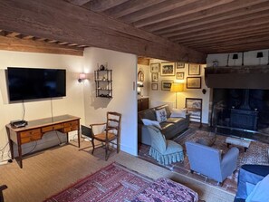 A cozy living room with a wooden ceiling, a flat-screen TV, a desk, a comfortable sofa, and a fireplace.