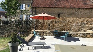 Eine Terrasse im Freien mit Steinmauern, einem Tisch, Stühlen und einem großen Sonnenschirm.