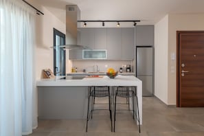 A modern kitchen with a central island, bar stools, a refrigerator, and a coffee maker.