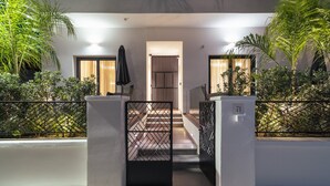 Een modern gebouwde ingang met een trap naar een deur, omringd door groen en een metalen hek.