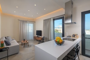 A modern kitchen with a central island, a dining area with a sofa and a small table, and a living area with a TV and a plant.