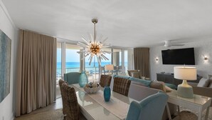 A hotel room with a dining area, a sofa, a TV, and a view of the ocean. - Experience luxury in this 3-bedroom oceanfront condo in Panama City Beach. (Panama City Beach)