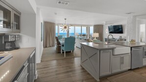 A modern hotel room with a kitchen, dining area, and a large window offering a view of the sea. - Experience luxury in this 3-bedroom oceanfront condo in Panama City Beach. (Panama City Beach)