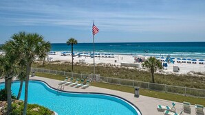A pool area with lounge chairs, a flag, and a beach in the background. - Experience luxury in this 3-bedroom oceanfront condo in Panama City Beach. (Panama City Beach)