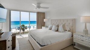 A hotel room with a large bed, a ceiling fan, a view of the beach, and a nightstand with a lamp. - Experience luxury in this 3-bedroom oceanfront condo in Panama City Beach. (Panama City Beach)