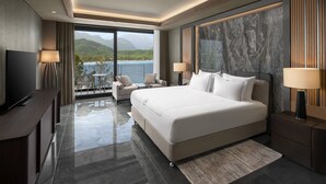 Une chambre d’hôtel moderne dotée d’un grand lit, d’une télévision, d’un balcon offrant une vue sur la mer et les montagnes, et d’un sol en marbre.