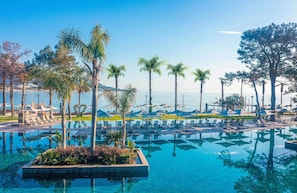A pool area with lounge chairs and umbrellas, surrounded by palm trees and a view of the sea. - NG Phaselis Bay - All inclusive (Kemer)