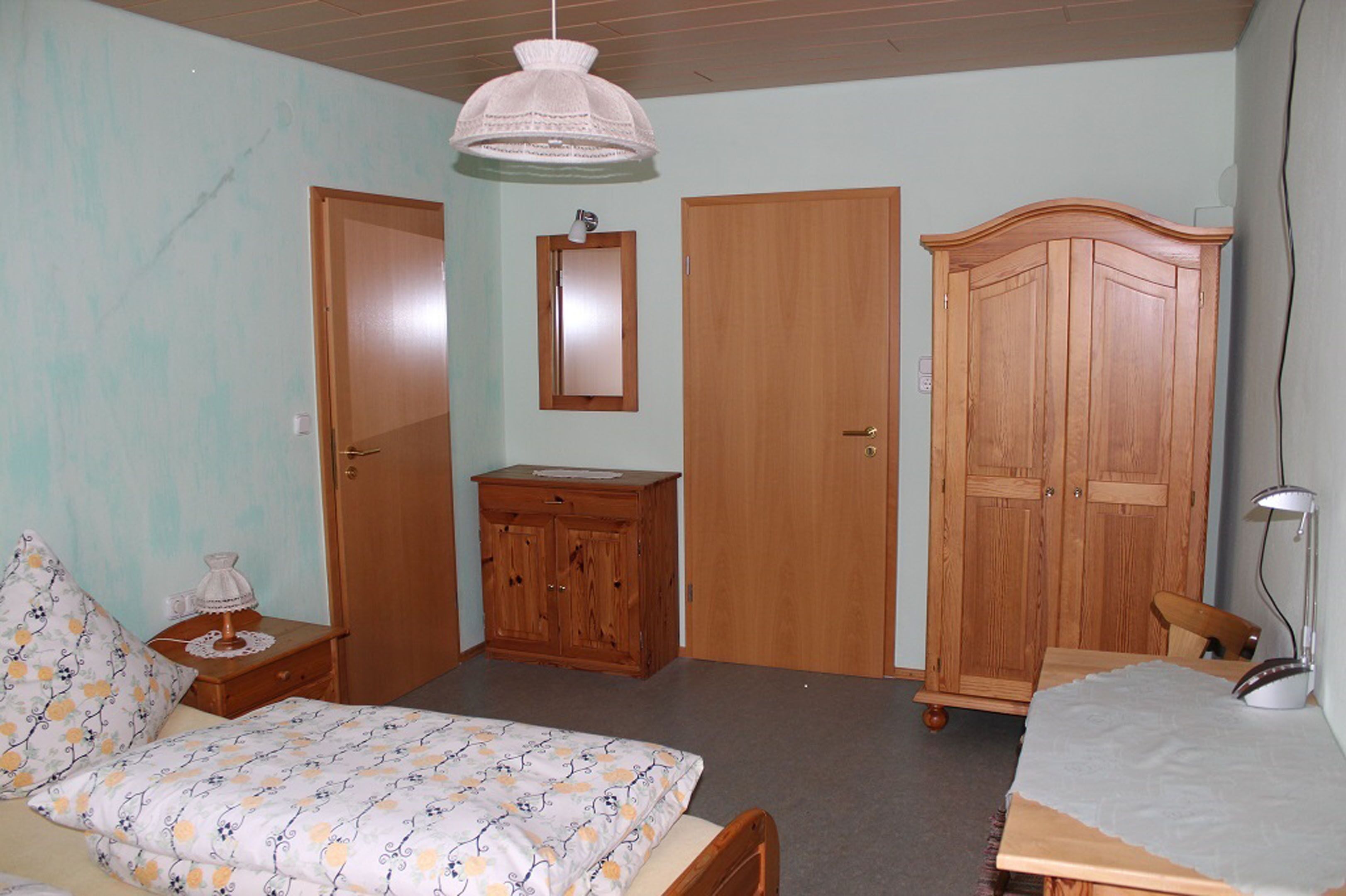 Un dormitorio con cama, armario de madera, mesita de noche, escritorio y silla.