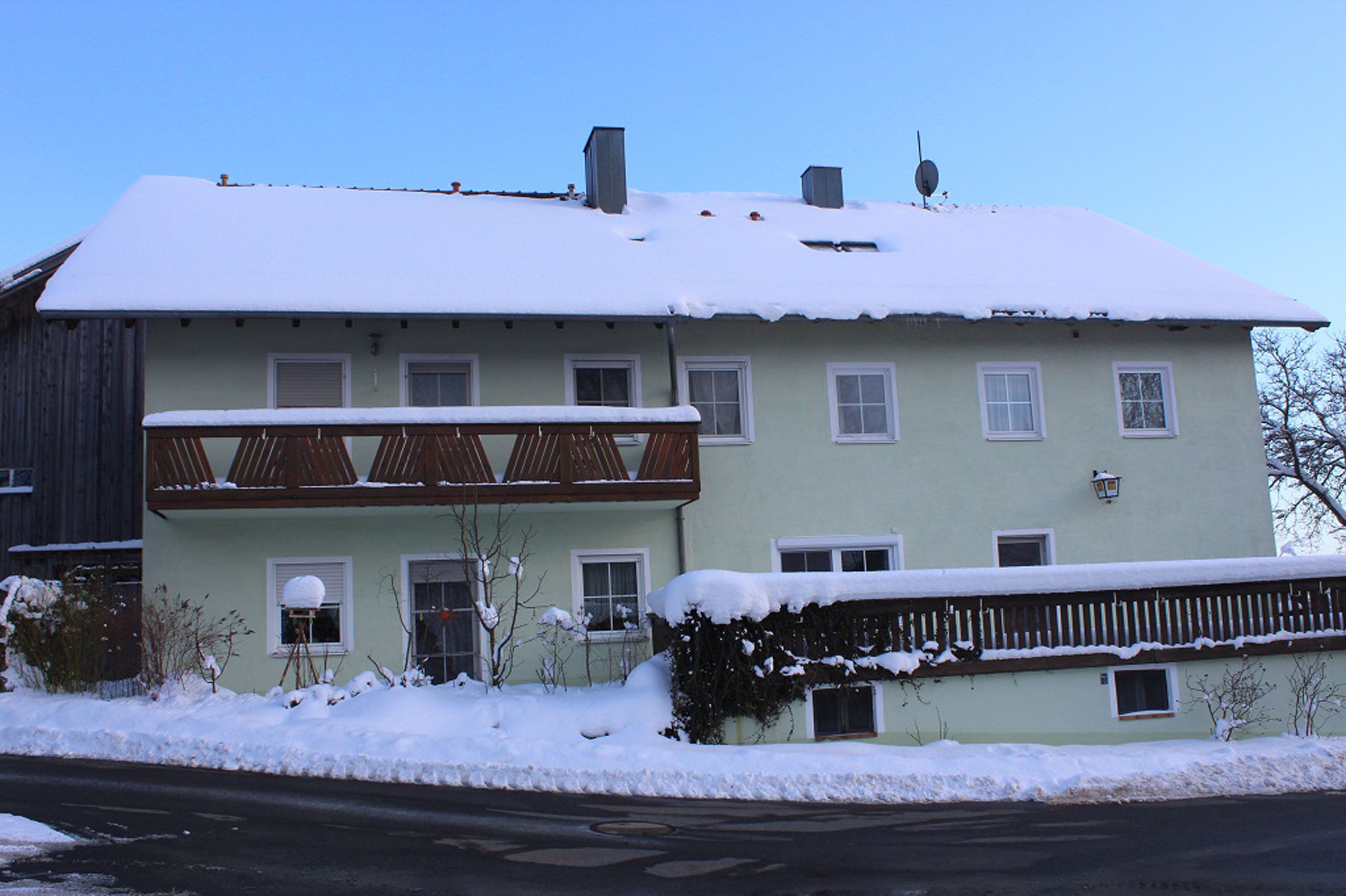 A two-story house with a balcony, surrounded by snow.