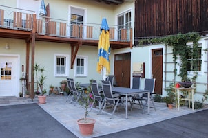 Un patio al aire libre con una mesa y sillas, plantas en macetas y una barandilla de madera en el balcón.