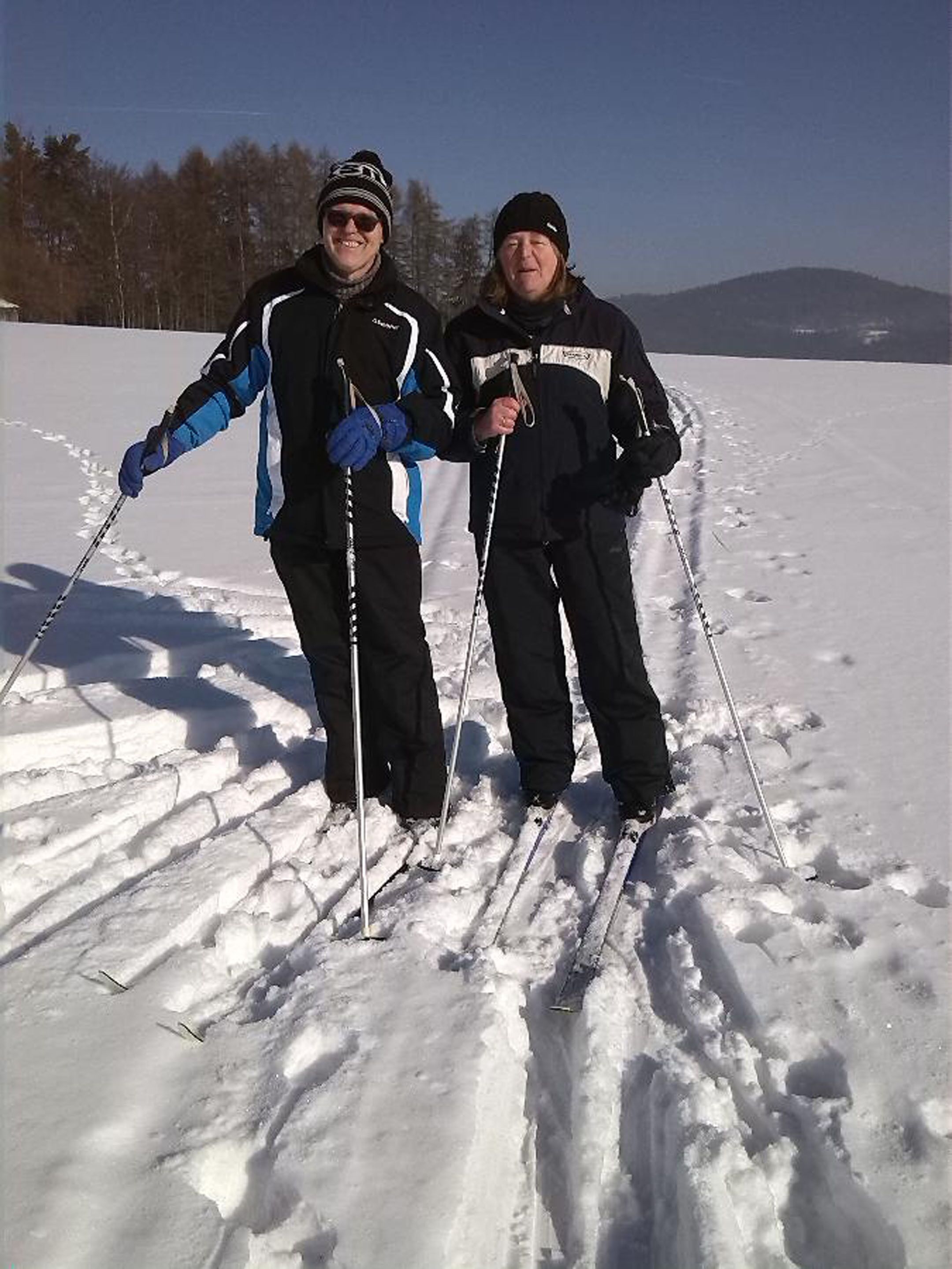 Two people cross-country skiing on a snowy field with a clear sky.