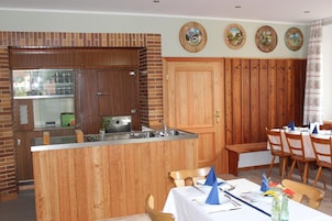 Una cocina con armarios de madera, un lavamanos integrado y una zona de comedor con una mesa preparada para cuatro comensales.