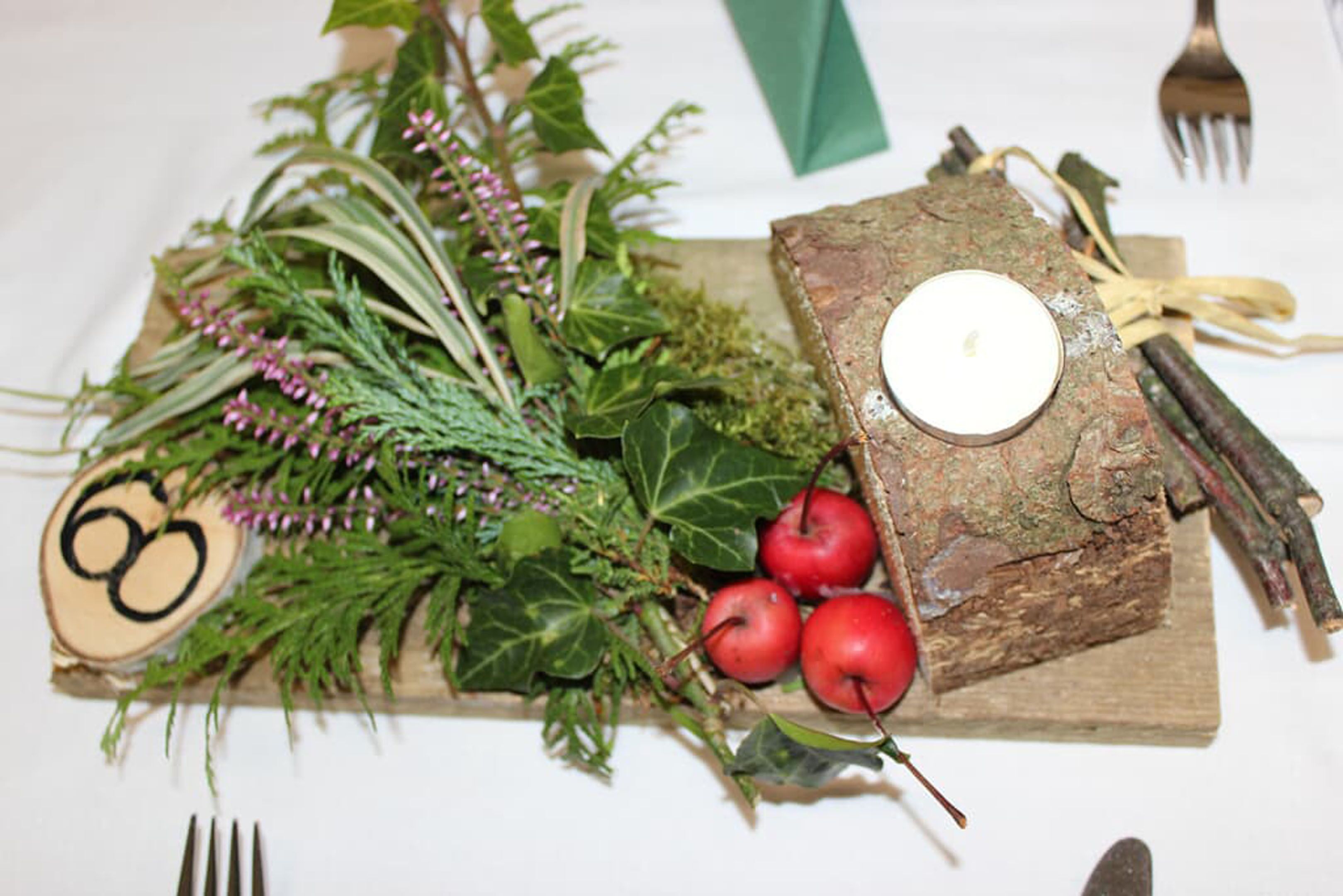 Une planche en bois rustique, ornée d’une bougie, de pommes rouges et de feuillage vert.