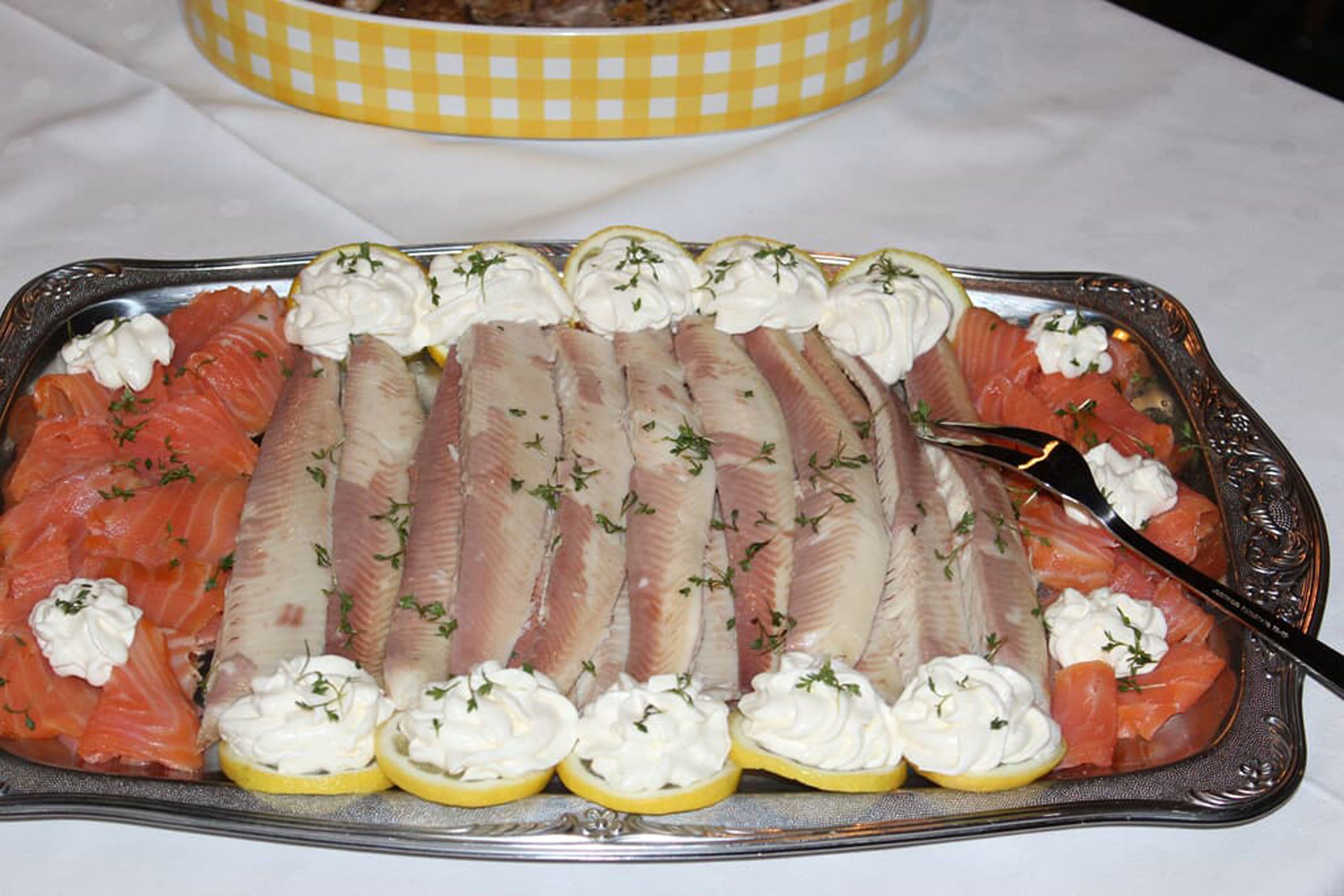 Una bandeja con salmón ahumado y pescado decorados con crema y hierbas, con un gajo de limón y un tenedor.
