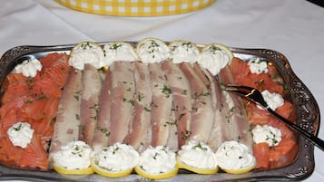 Una bandeja con salmón ahumado y pescado decorados con crema y hierbas, con un gajo de limón y un tenedor.
