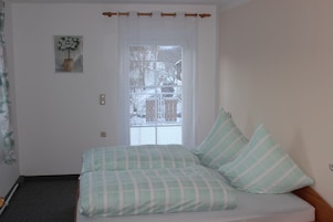Un dormitorio con cama, ventana con vistas a árboles y puerta con cortina.