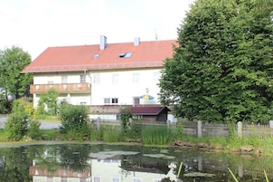 A residential building with a red-tiled roof, a balcony, and a small garden area with a pond.