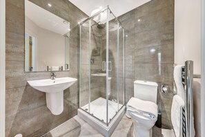 A modern bathroom with a glass-enclosed shower, a pedestal sink, and a toilet. - Paladin Place (Redhill)