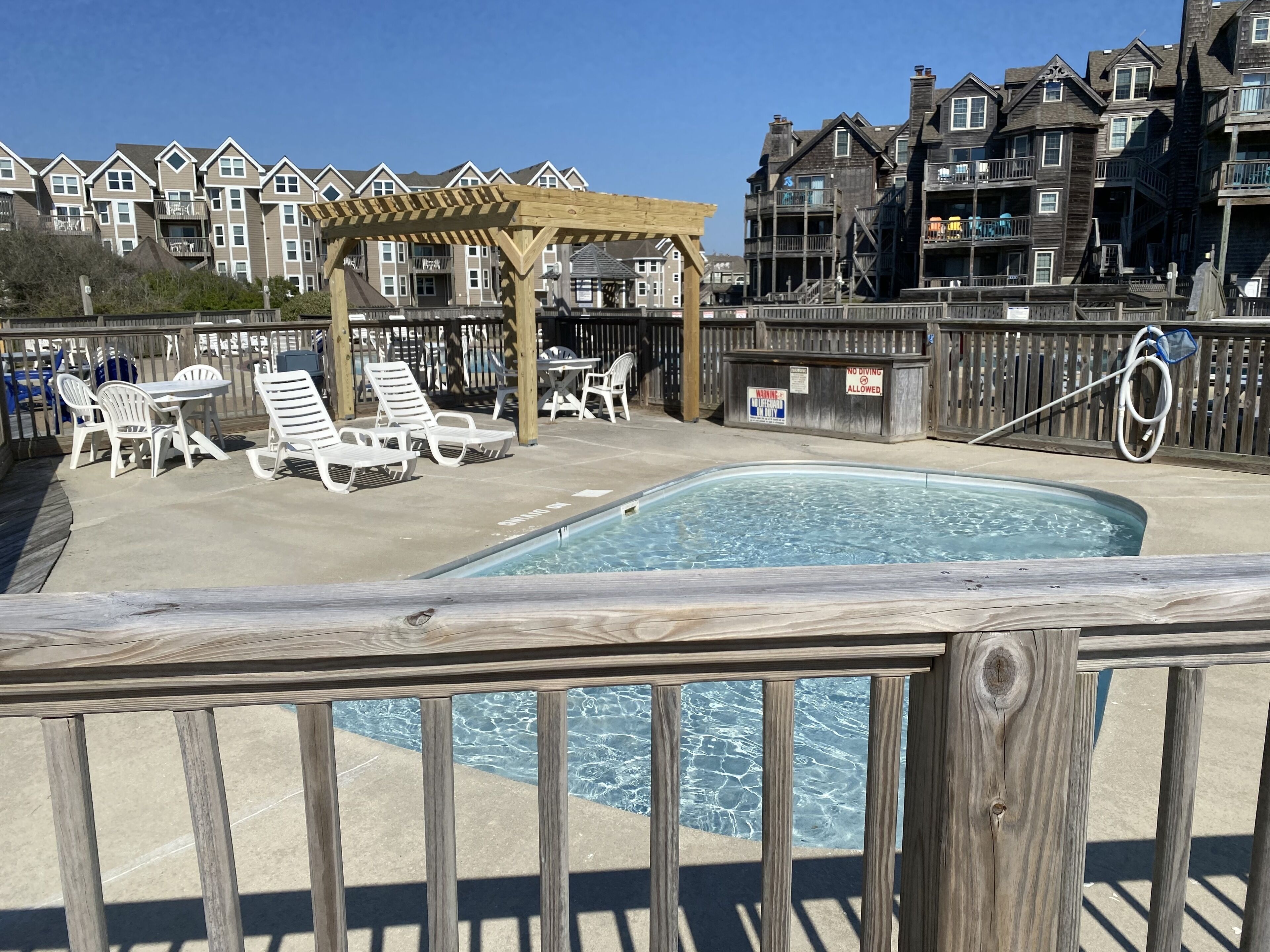 A pool area with lounge chairs and a wooden pergola.